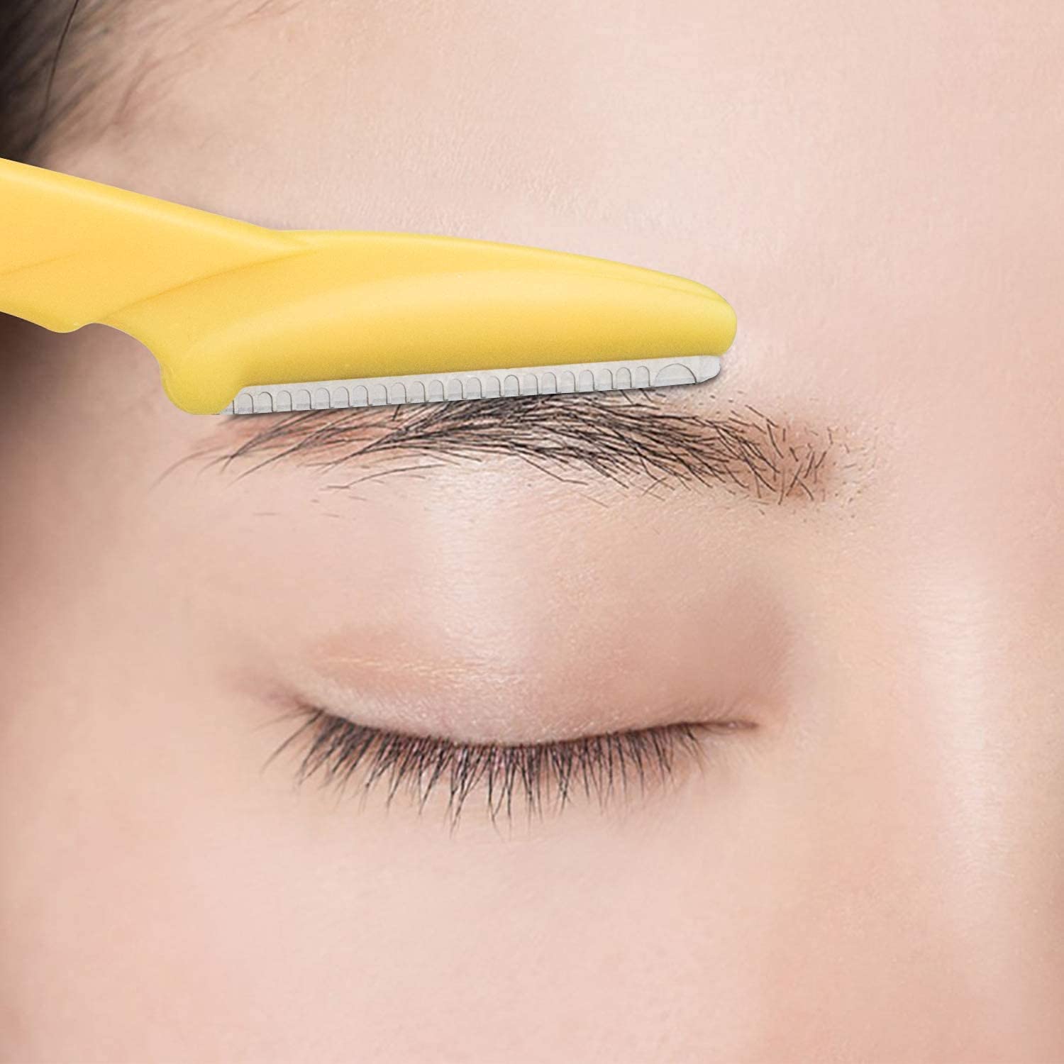 Close up of a yellow eyebrow razor trimming a natural eyebrow on smooth skin eyebrow razor for women and men Close up of a yellow eyebrow razor trimming a natural eyebrow on smooth skin eyebrow razor for women and men
