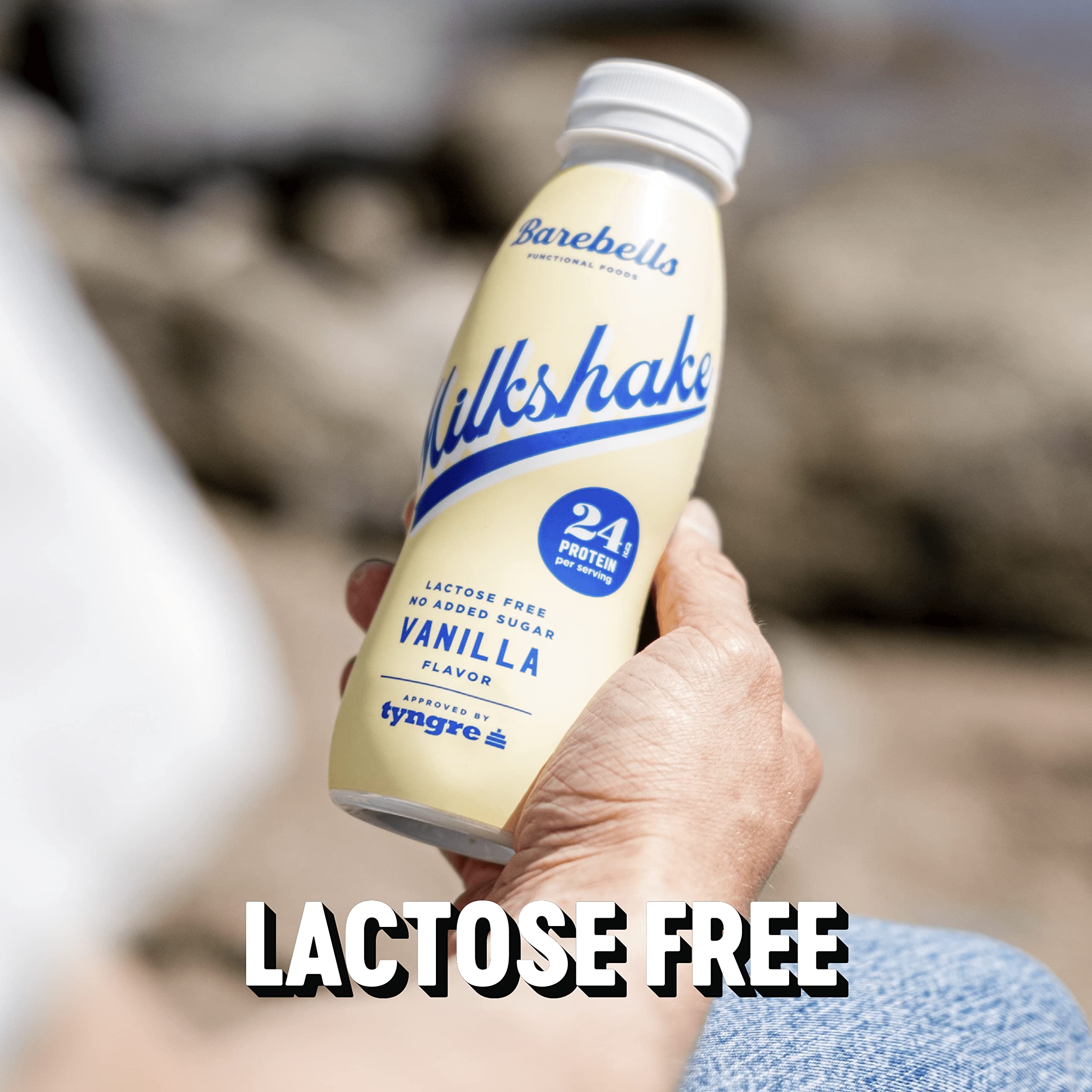 Hand holding Barebells protein milkshake vanilla bottle outdoors showing 24g protein and lactose free label Hand holding Barebells protein milkshake vanilla bottle outdoors showing 24g protein and lactose free label