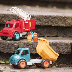 Battat dump truck toy for kids in yellow and blue with red fire truck and two toy figures on stone steps Battat dump truck toy for kids in yellow and blue with red fire truck and two toy figures on stone steps