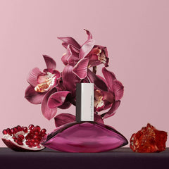Calvin Klein Euphoria perfume for women with purple bottle, orchids, pomegranate, and amber on pink background Calvin Klein Euphoria perfume for women with purple bottle, orchids, pomegranate, and amber on pink background