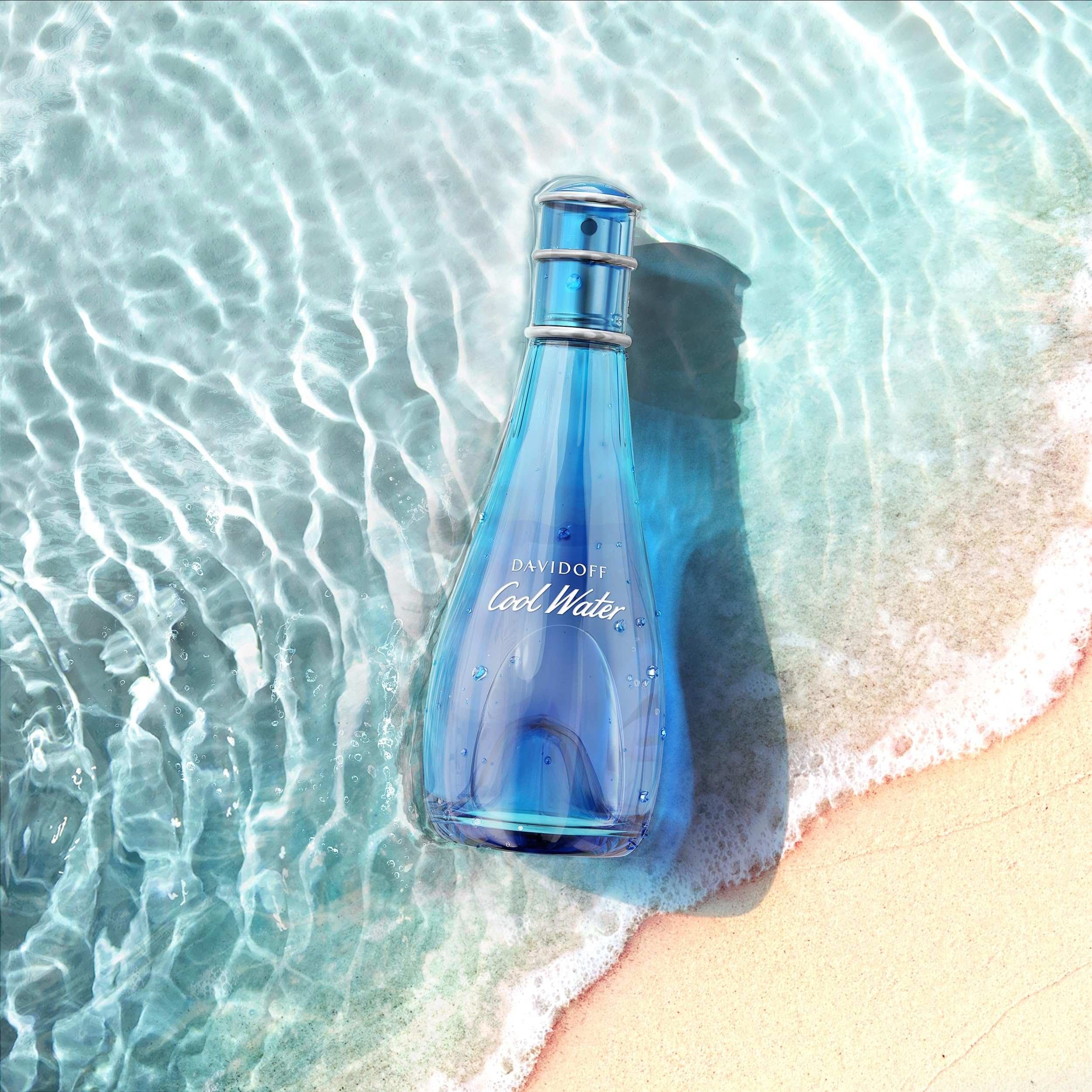 Davidoff Cool Water perfume for women blue bottle resting on beach sand with ocean waves Davidoff Cool Water perfume for women blue bottle resting on beach sand with ocean waves