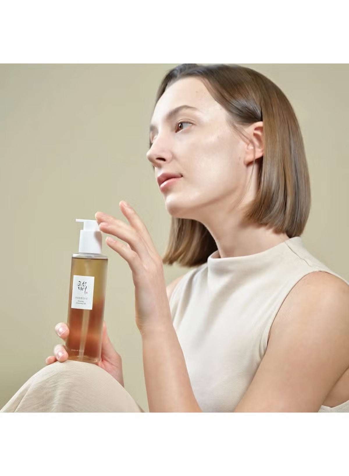 Beauty of Joseon ginseng cleansing oil in a clear bottle held by a woman with a natural look Beauty of Joseon ginseng cleansing oil in a clear bottle held by a woman with a natural look