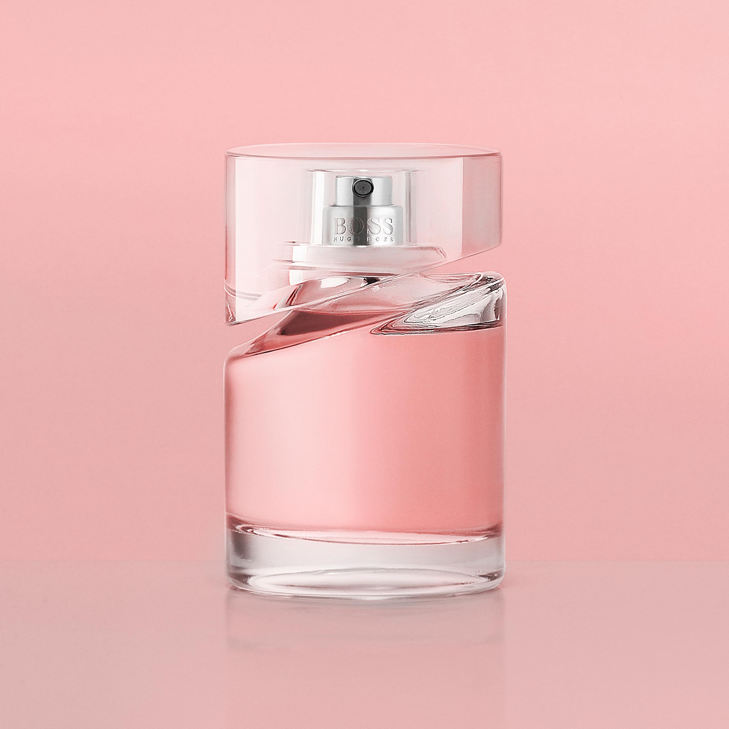Clear glass bottle of Hugo Boss Femme perfume with pink fragrance against a soft pink background Clear glass bottle of Hugo Boss Femme perfume with pink fragrance against a soft pink background