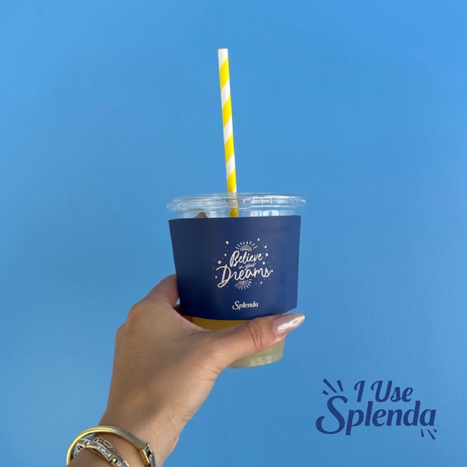 Hand holding iced drink with navy Splenda sleeve and yellow straw featuring Splenda no calorie sweetener packets logo Hand holding iced drink with navy Splenda sleeve and yellow straw featuring Splenda no calorie sweetener packets logo
