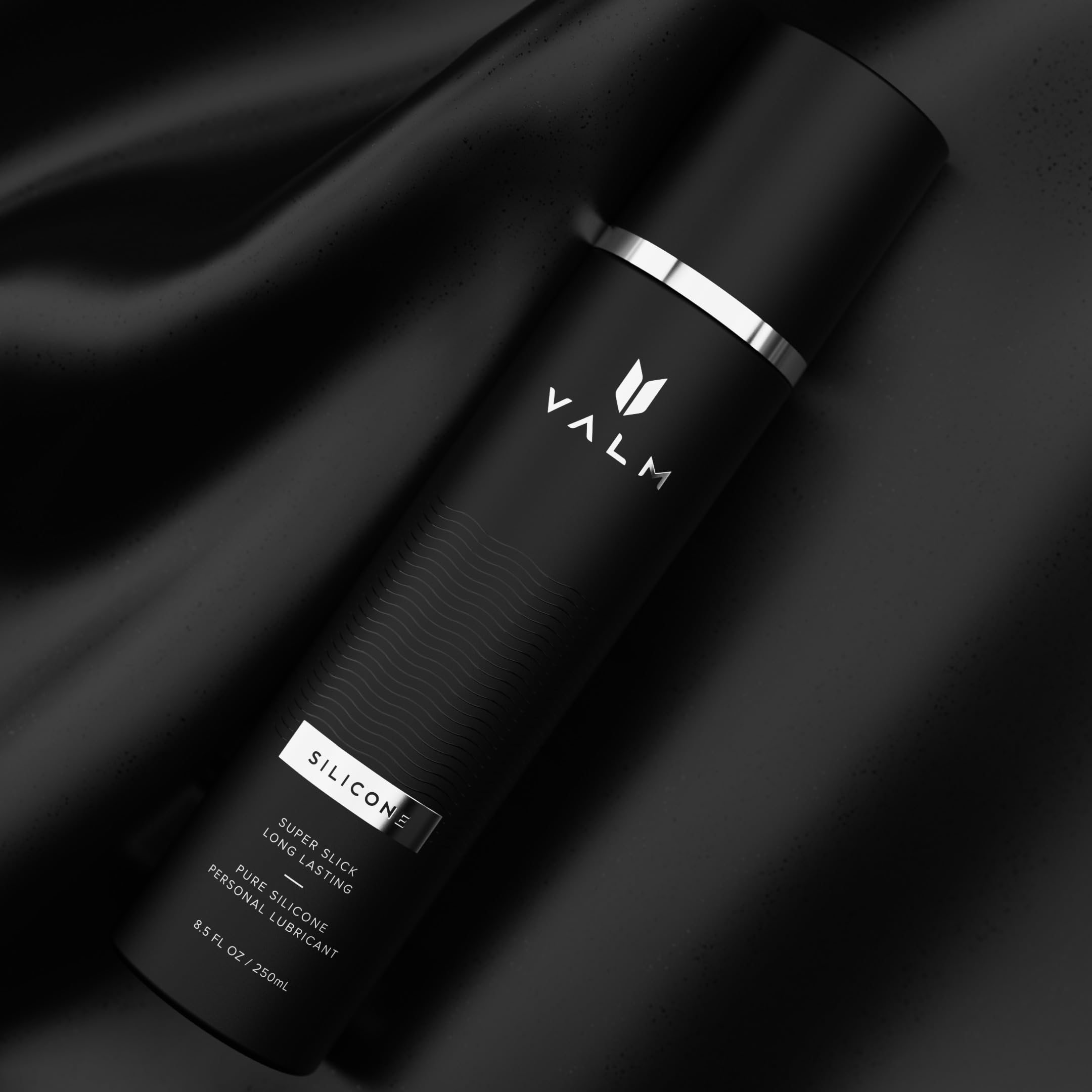 Valm black premium bottle of silicone based personal lubricant with sleek matte packaging on black satin Valm black premium bottle of silicone based personal lubricant with sleek matte packaging on black satin