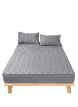 Dark grey fitted bedding topper with two quilted pillowcases on a bed