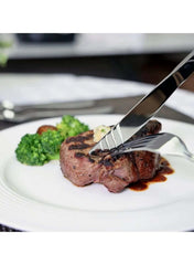 24 piece stainless steel flatware set by Huitich cutting a cooked steak with vegetables on a white plate