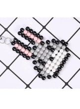 Water bead keychain or charm with black, pink, and white bead pattern on a grid