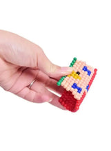 Water bead craft piece held in a hand, with colorful pixel pattern on the grid