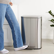 Stainless steel kitchen bin with pedal and closed lid, satin nickel finish, near person.