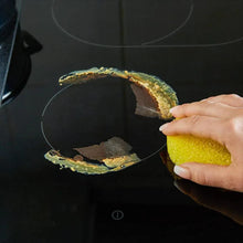 Yellow sponge removing grime from a black stovetop pan edge