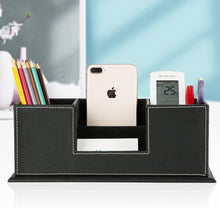 Black PU leather desk organizer with four compartments holding phone, calculator, pens, and remote