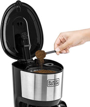 Black+Decker drip coffee maker with open top and glass carafe, hand adding coffee grounds