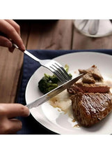 Stainless steel dinner knife cutting steak on a plate, held with a fork.