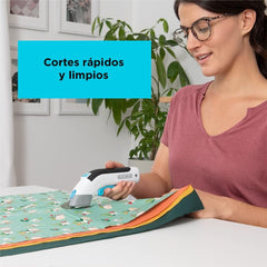 Cordless electronic scissors with white body and blue handle cutting colorful fabric on table