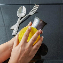 Hands wiping a metal cup with a yellow sponge