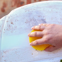 Hand using a yellow sponge on a white surface with visible stains