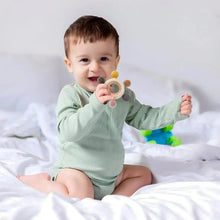 Baby holding a pink and gray silicone teething toy with a wooden ring