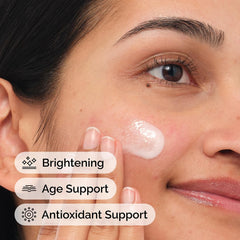 Woman applying brightening face cream to cheek with visible glow and benefits labels The Ordinary Vitamin C Suspension .