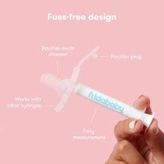 Frida Baby MediFrida Accu-Dose Pacifier held in hand on pink background showing pacifier plug and dosing syringe
