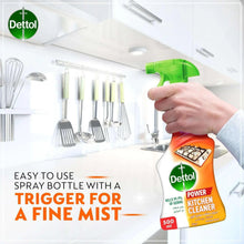 Hand holding orange Dettol kitchen cleaner spray bottle with green trigger and mist