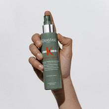 Hand holding Kerastase Genesis Homme thickening hair spray bottle with pump