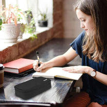Black pencil bag on desk next to an open notebook while writing