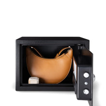 Black security safe with hinged door open, showing tan bag inside