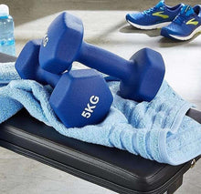 Blue 5KG neoprene dumbbells resting on a workout bench with towel.