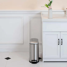 Brushed stainless steel trash can with closed lid and black foot pedal on floor