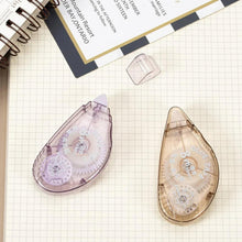 Two translucent double sided tape applicators in lavender and beige on grid paper