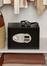 Black security safe with digital keypad, positioned on a shelf with glasses above