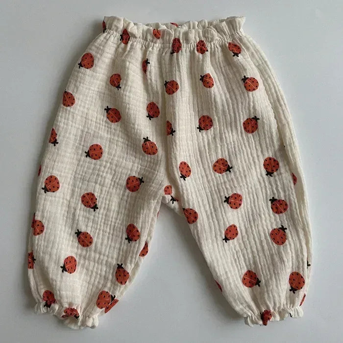 White muslin baby pants covered in red ladybugs, elastic waist and cuffs