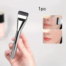 Oval foundation brush with fine dark bristles and shiny silver handle, held in hand