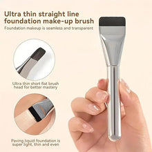 Straight-line foundation brush with silver handle and black flat bristles, held by hand