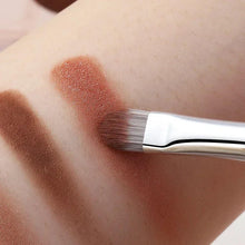 Makeup brush applying brown eyeshadow to skin swatch