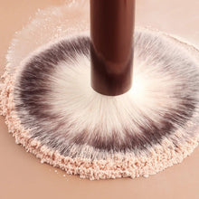 Powder makeup brush with thick round bristles applying product on a light powder surface