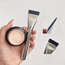Foundation brush with silver handle and black bristles, held in hand for liquid makeup