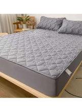 Dark grey fitted bedding topper on mattress with matching pillowcases, angled view