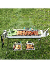 Portable BBQ grill on grass with skewers and food cooking on wire grates