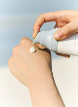 Hand dispensing a small dollop from a white sunscreen tube onto skin