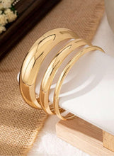 Gold tone bangle bracelet set on wooden stand, three shiny cuffs