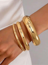 Gold tone bangle bracelet set on wrist, three stacked wide cuffs