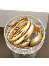 Gold tone bangle bracelet set in clear cup, three reflective cuffs