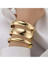 Gold tone bangle bracelet set on wrist, three stacked polished cuffs