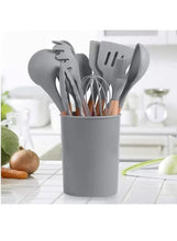 Grey silicone kitchen utensil set with wooden handles stored in a matching cup