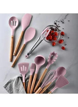 Pink silicone cooking utensils set with wooden handles on countertop.