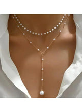 Layered pearl drop necklace worn with three layered pearl strands and center drop