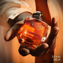 Emporio Armani men's eau de parfum bottle held in hands, orange liquid, black cap.