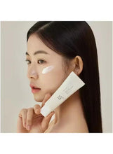Face sunscreen applied with white cream on cheek and temple; tube in hand.